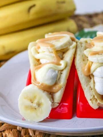 Pancakes filled with cheesecake mousse, bananas, and topped with caramel on a white plate.