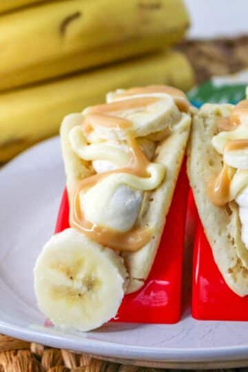 Pancakes filled with cheesecake mousse, bananas, and topped with caramel on a white plate.