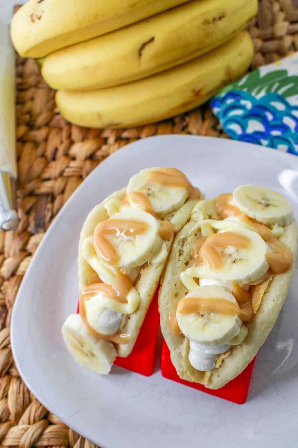 Pancakes filled with cheesecake mousse, bananas, and topped with caramel on a white plate. 