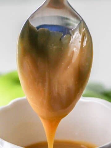 Dulce de Leche dripping from a spoon over a white cup.