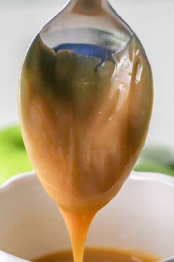 Dulce de Leche dripping from a spoon over a white cup.