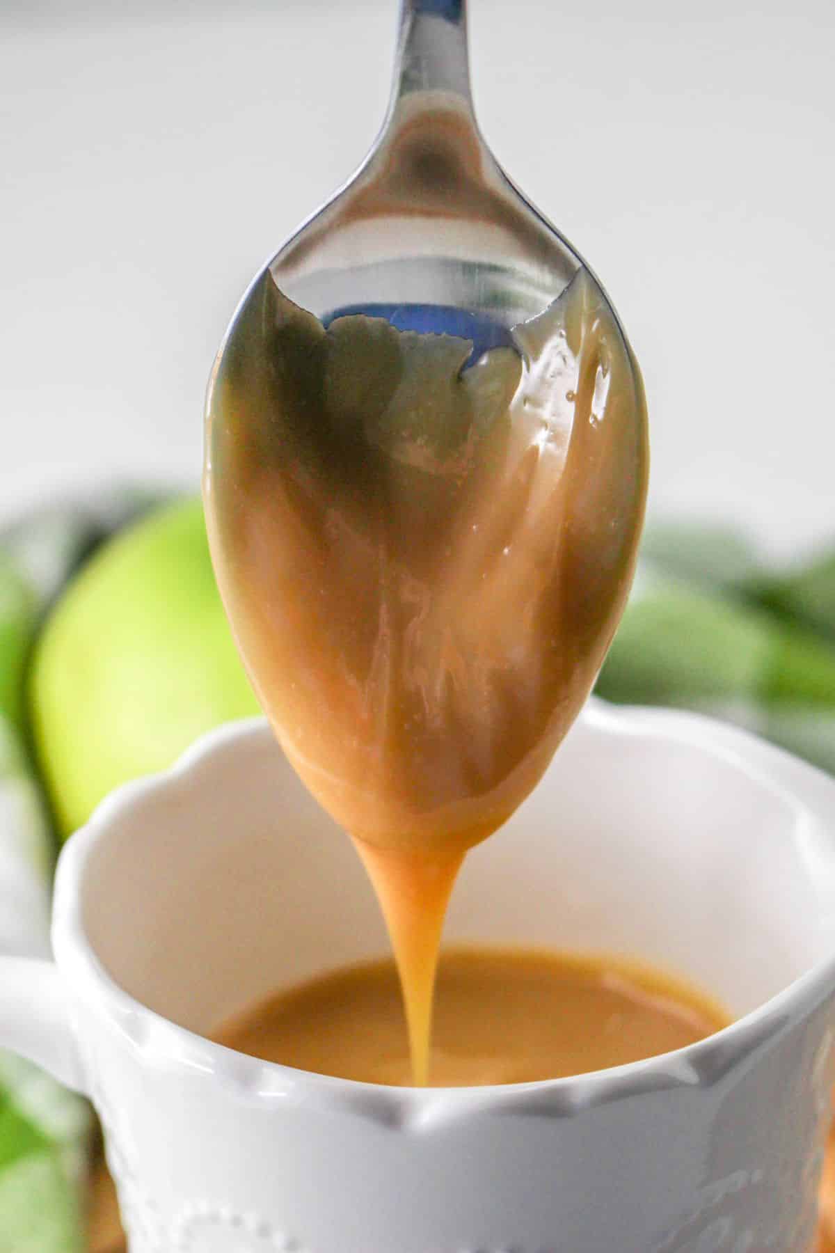 Dulce de Leche dripping from a spoon over a white cup. 