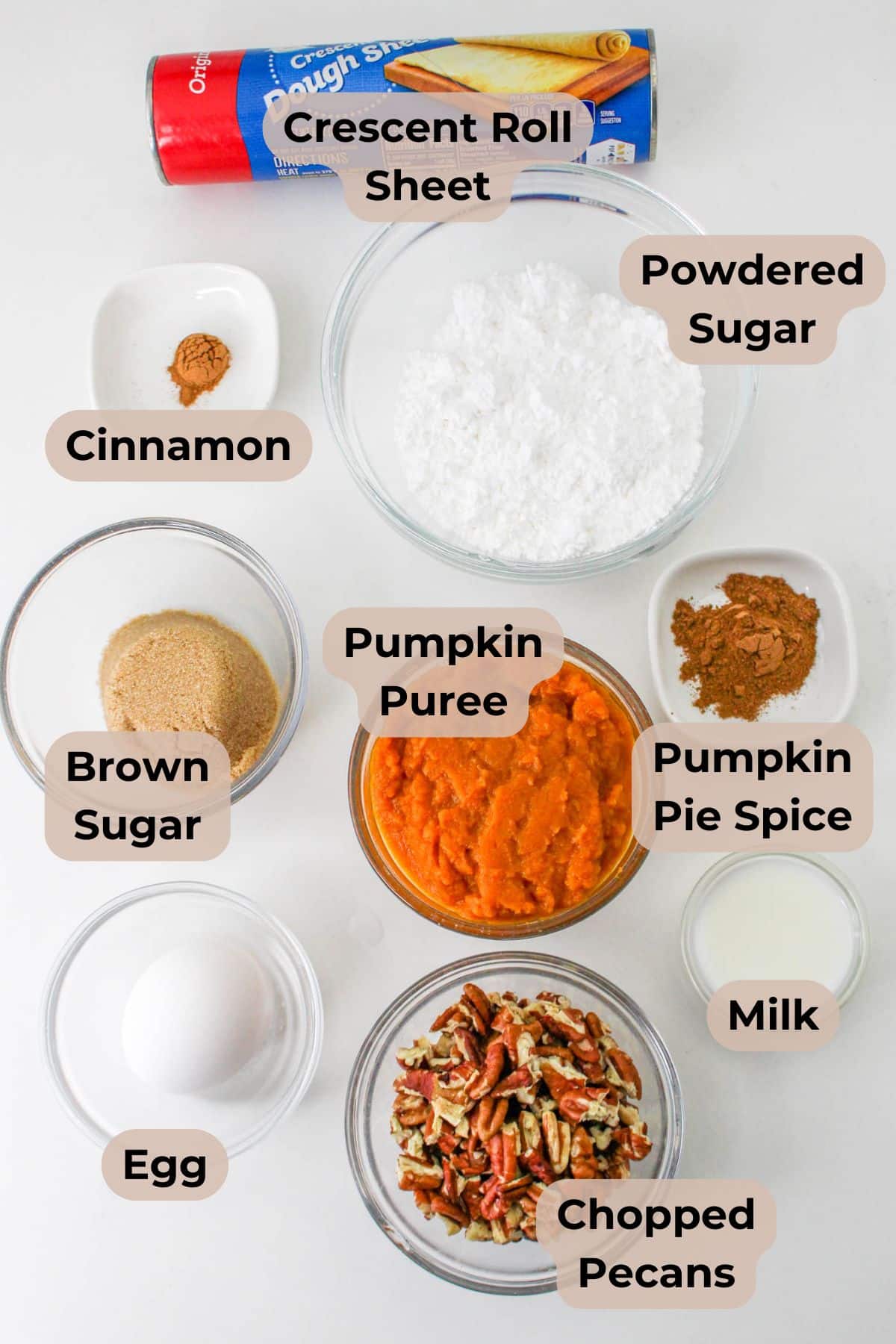 Baking ingredients on a white surface for a delicious pumpkin braid with pecans: crescent roll sheet, pumpkin puree, sugars, spices, egg, milk, and pecans.