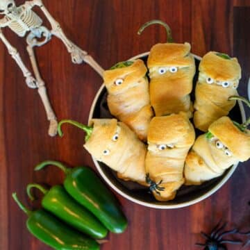Jalapeno poppers decorated as mummies in a metal pan on a table.
