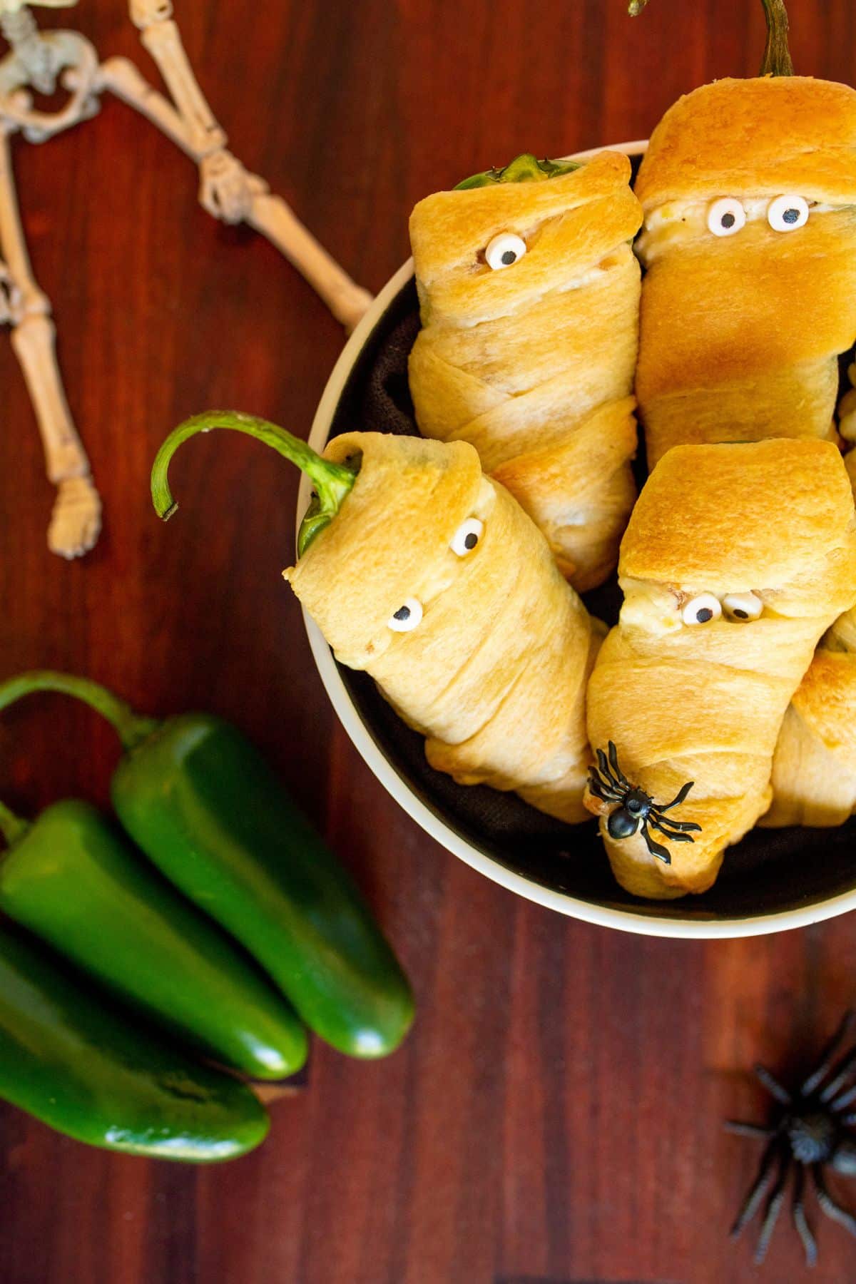 Jalapeno poppers decorated as mummies in a metal pan on a table.