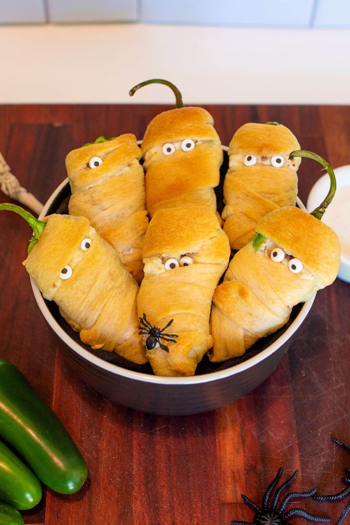 Jalapeno poppers decorated as mummies in a metal pan on a table. 