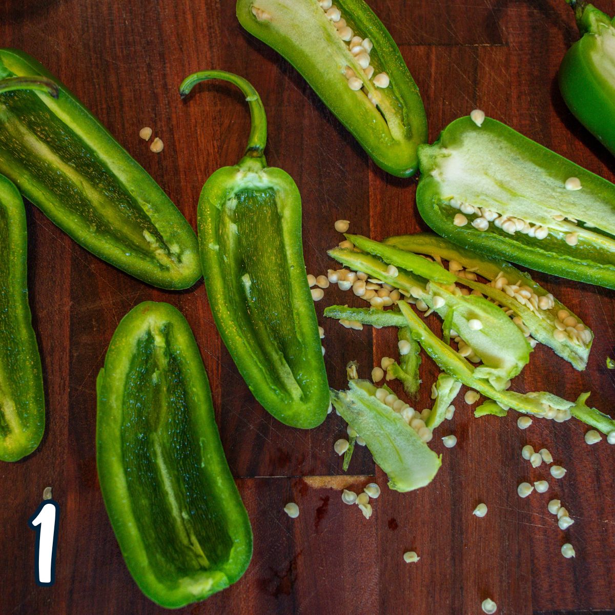 Jalapeno peppers cut in half with the seeds being removed on a cutting board. 