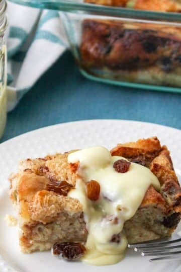A piece of bread pudding on a white plate next to a jar of vanilla sauce.