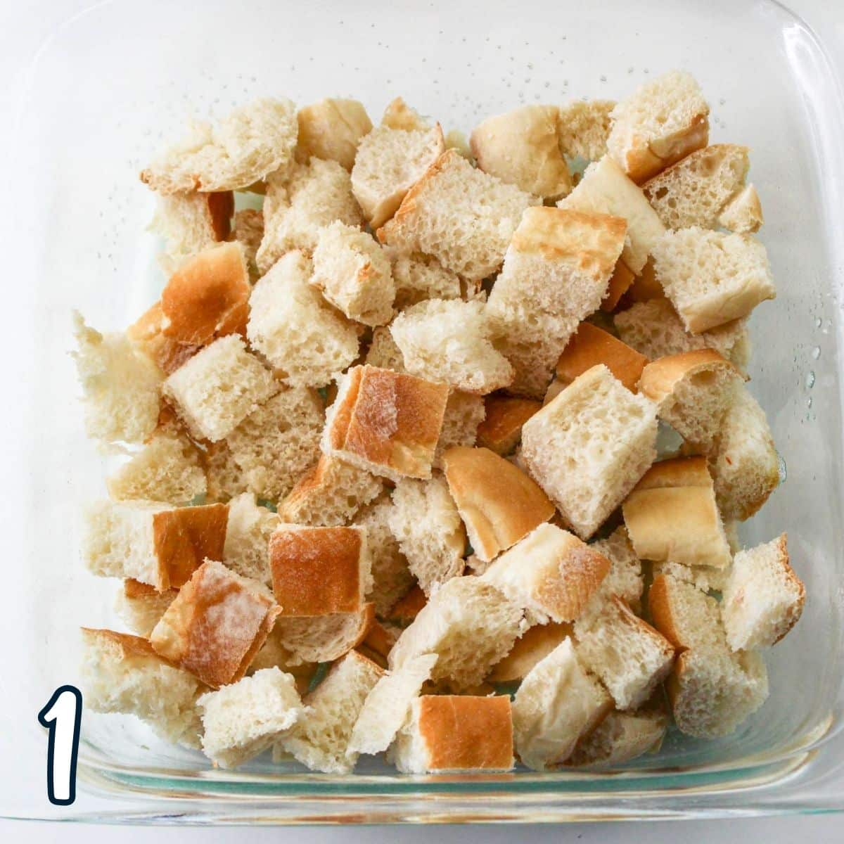 Bread cut into cubes in an 8 inch square baking dish. 