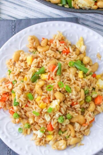 A white plate filled with cashew fried rice on a gray tablecloth.