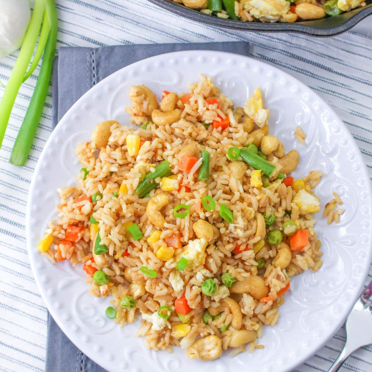 A white plate filled with cashew fried rice on a gray tablecloth.