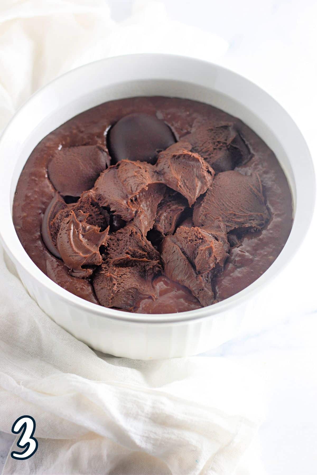 Chocolate frosting dabs on top of raw cake batter in a round baking dish. 