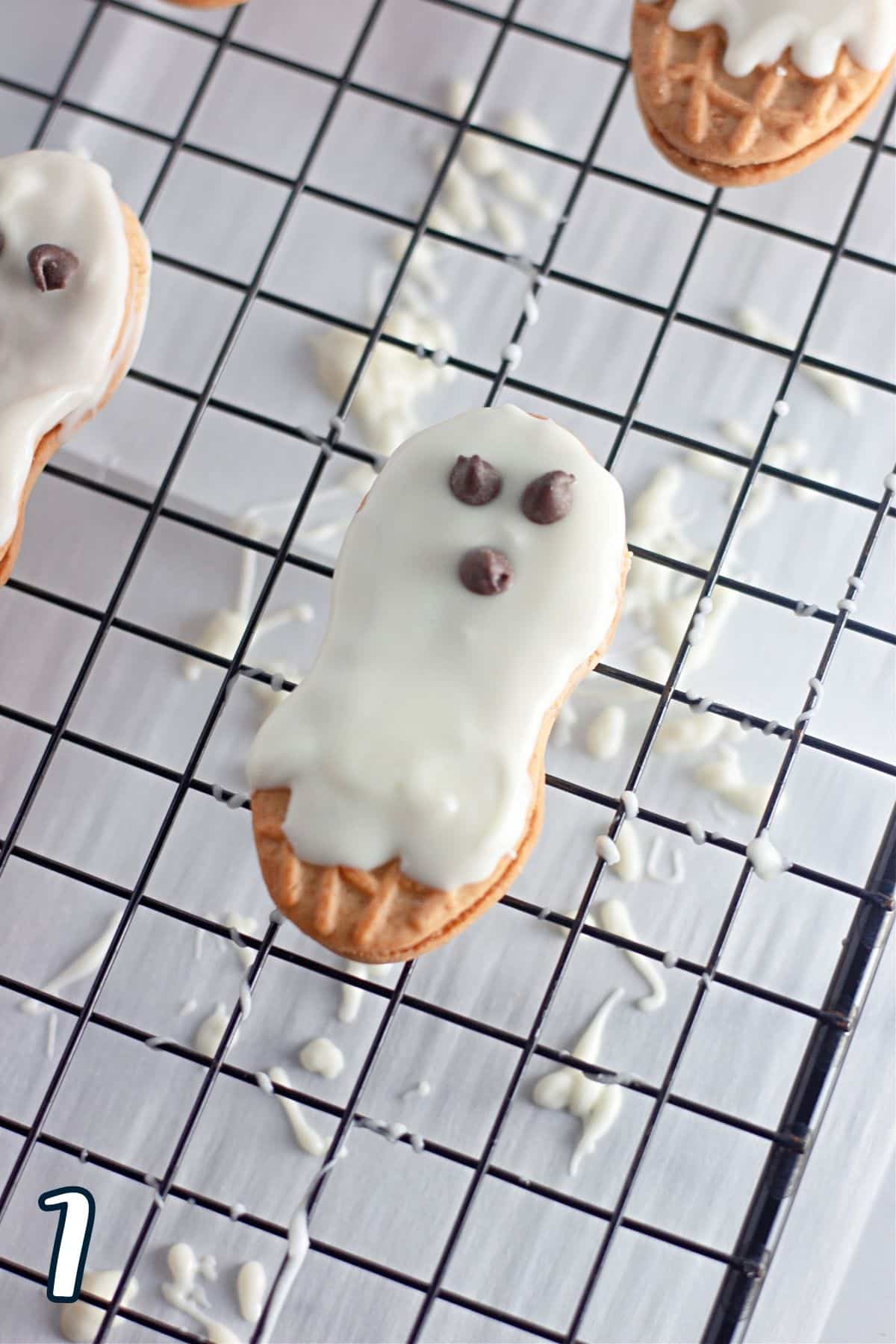 Mini chocolate chips used to make eyes and a mouth for a ghost on a cookie coated with white melting chocolate. 