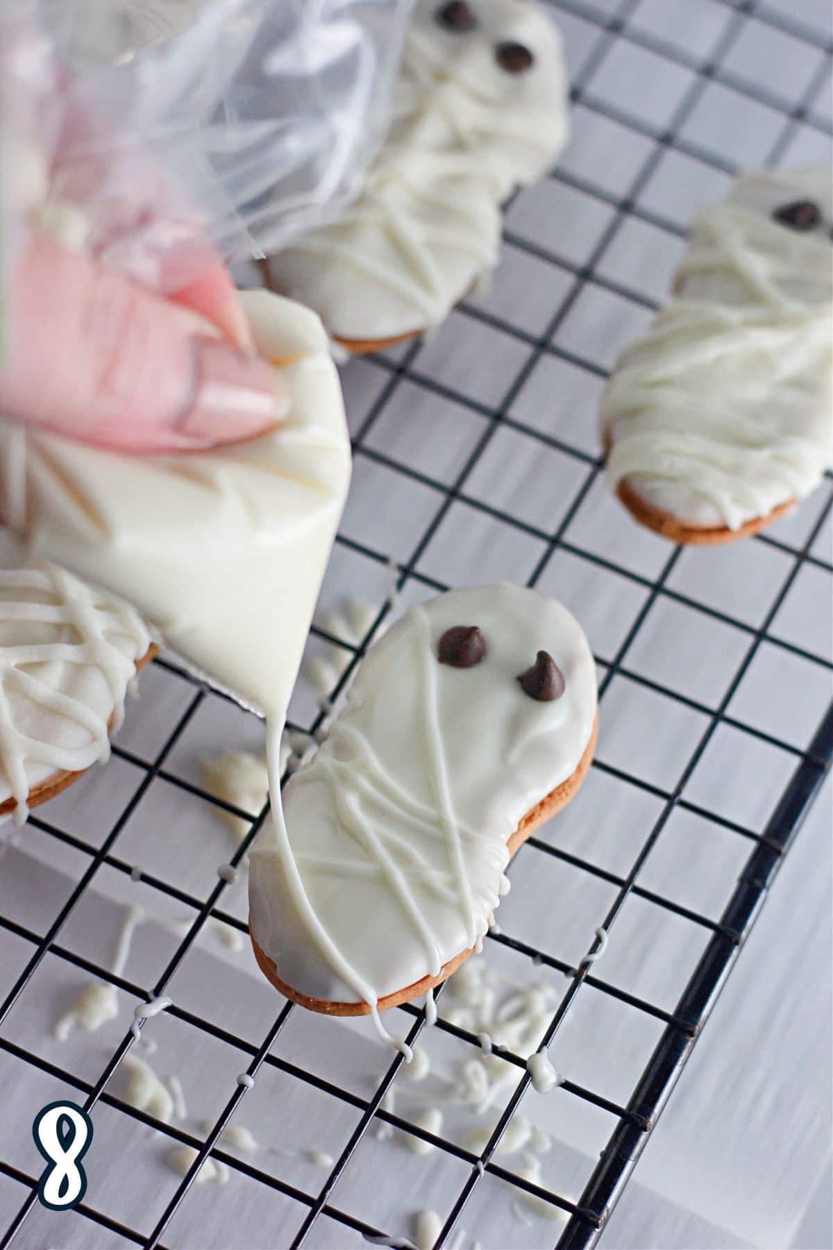 A piping bag of white chocolate being used to make a mummy out of a Nutter Butter cookies. 