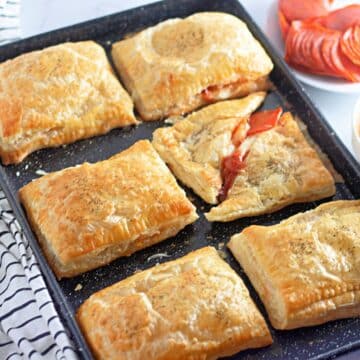 Golden brown puff pastry pockets on a black cookie sheet.