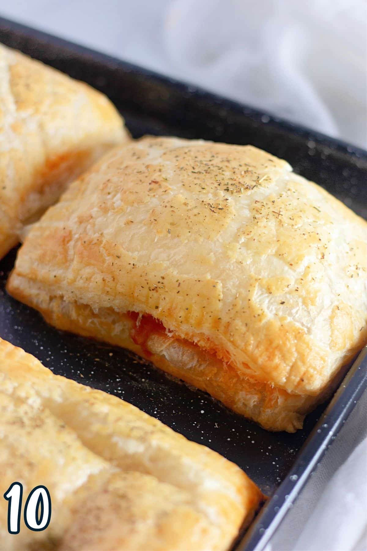 A pizza pocket made with puff pastry with pizza sauce dripping out on a baking sheet. 