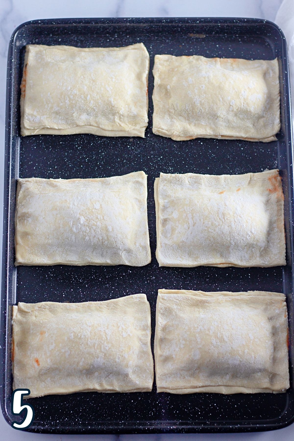 Six puff pastry pizza pockets on a baking sheet. 