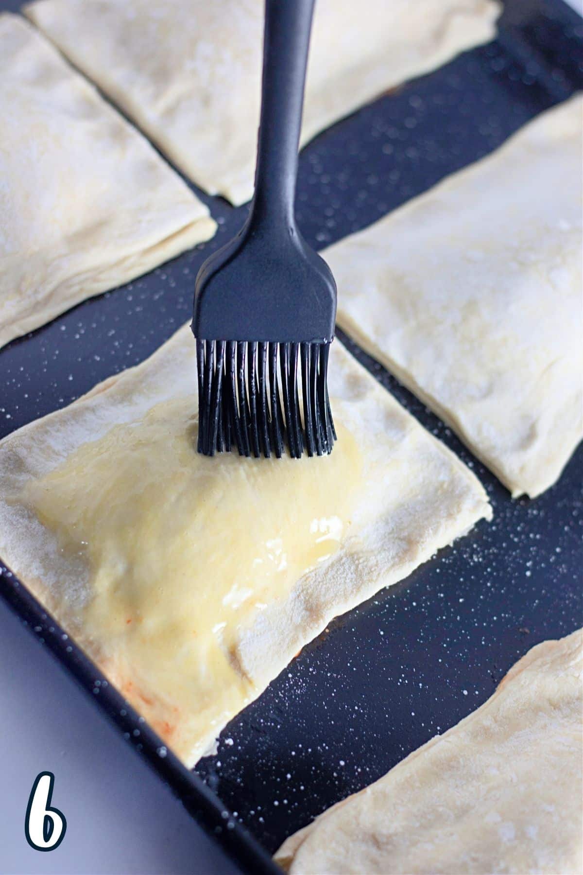 Egg wash being spread over puff pastry on a baking sheet. 