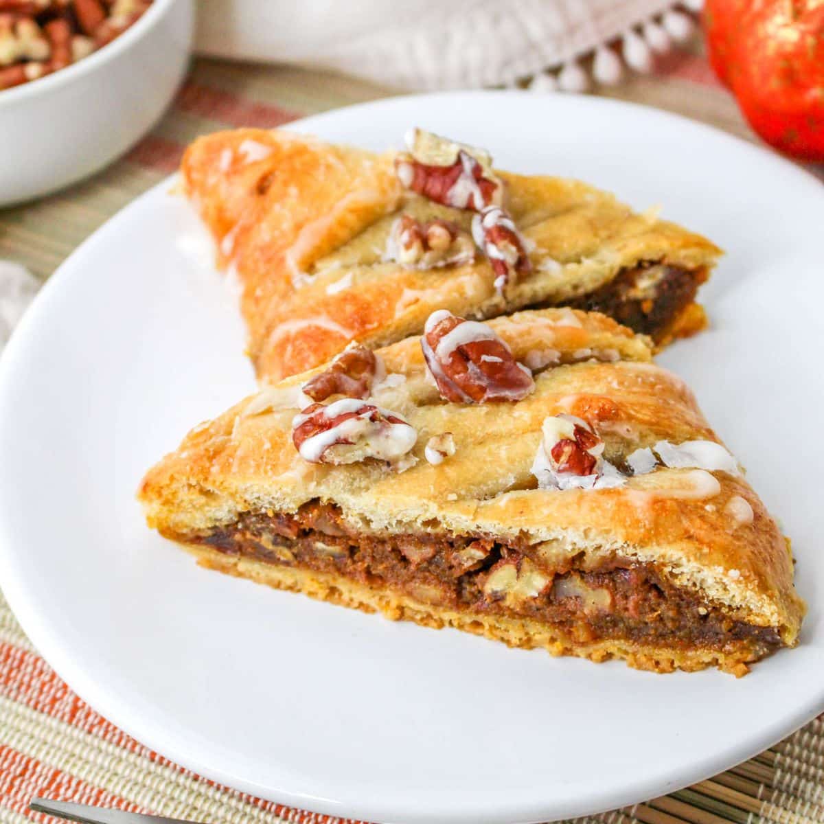 A piece of pumpkin pecan pastry on a white plate next to a white cup.