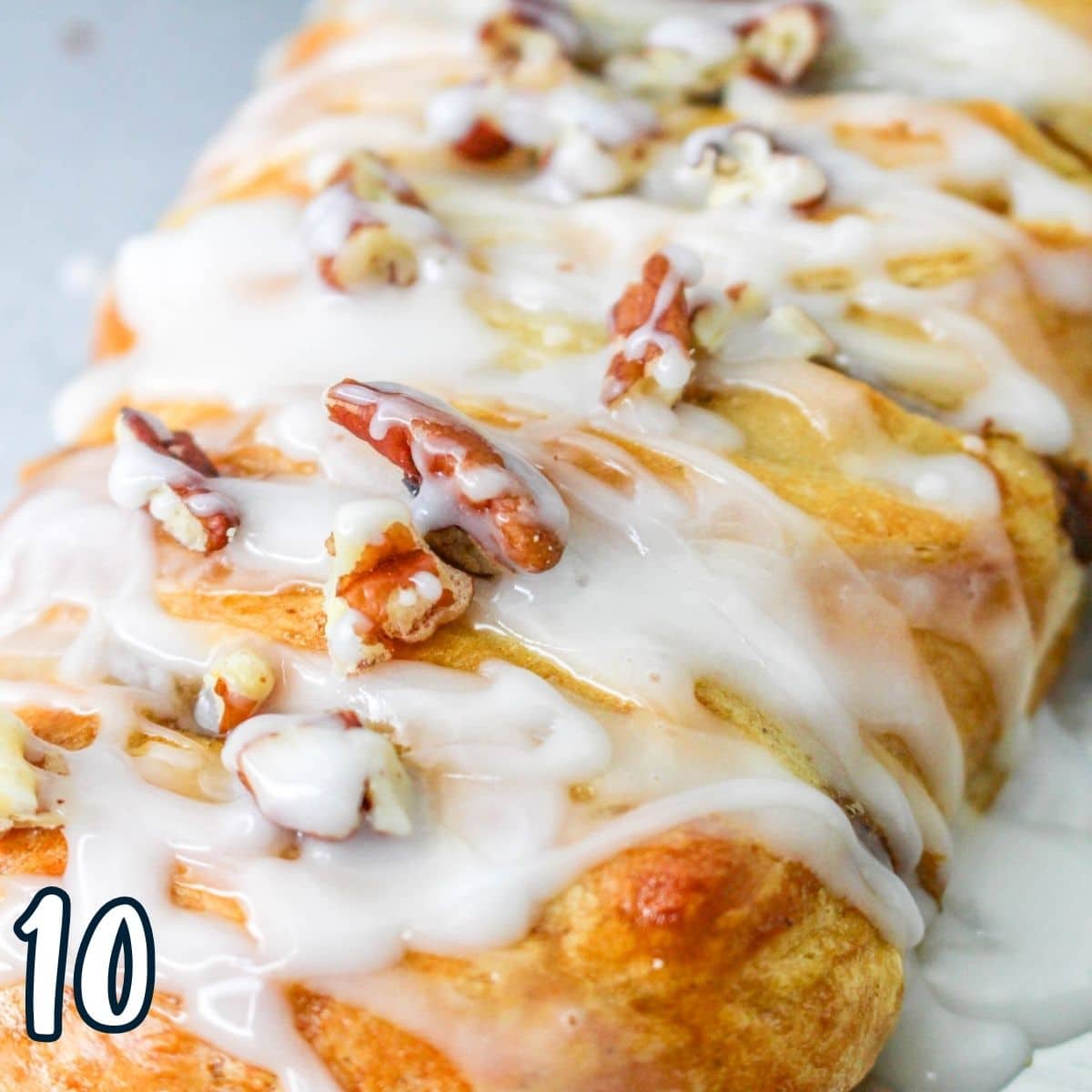 Glazed pumpkin braid topped with chopped pecans on a baking sheet. 