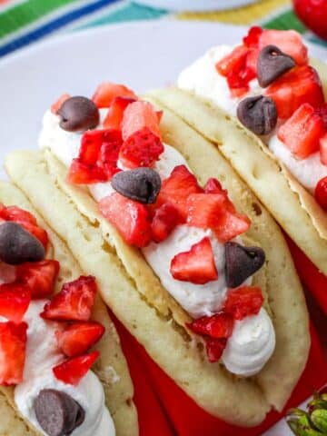 Pancakes filled with cheesecake mousse, strawberries, and chocolate chips in a red taco holder.