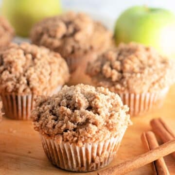 Apple cinnamon muffins on a cutting board with cinnamon sticks.
