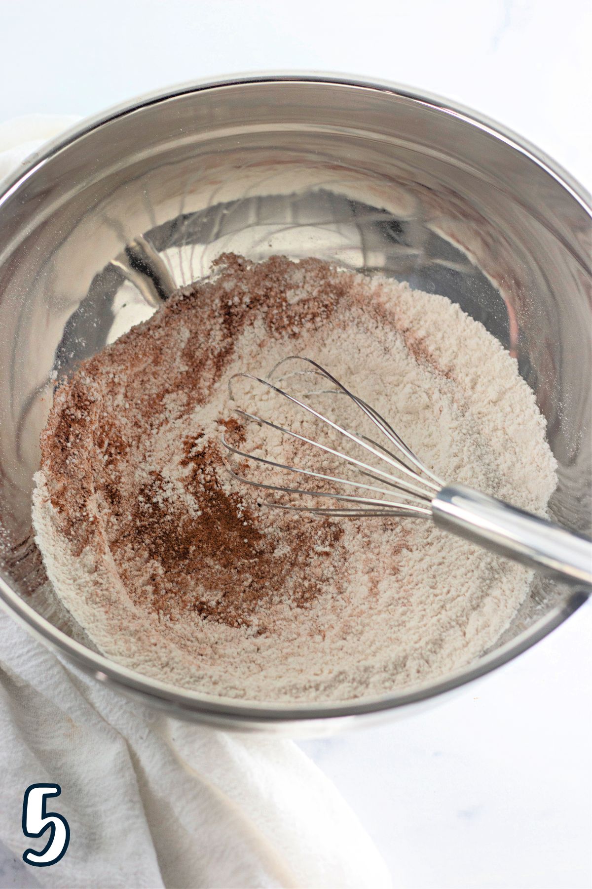 A bowl with flour, and other dry ingredients  and a whisk.