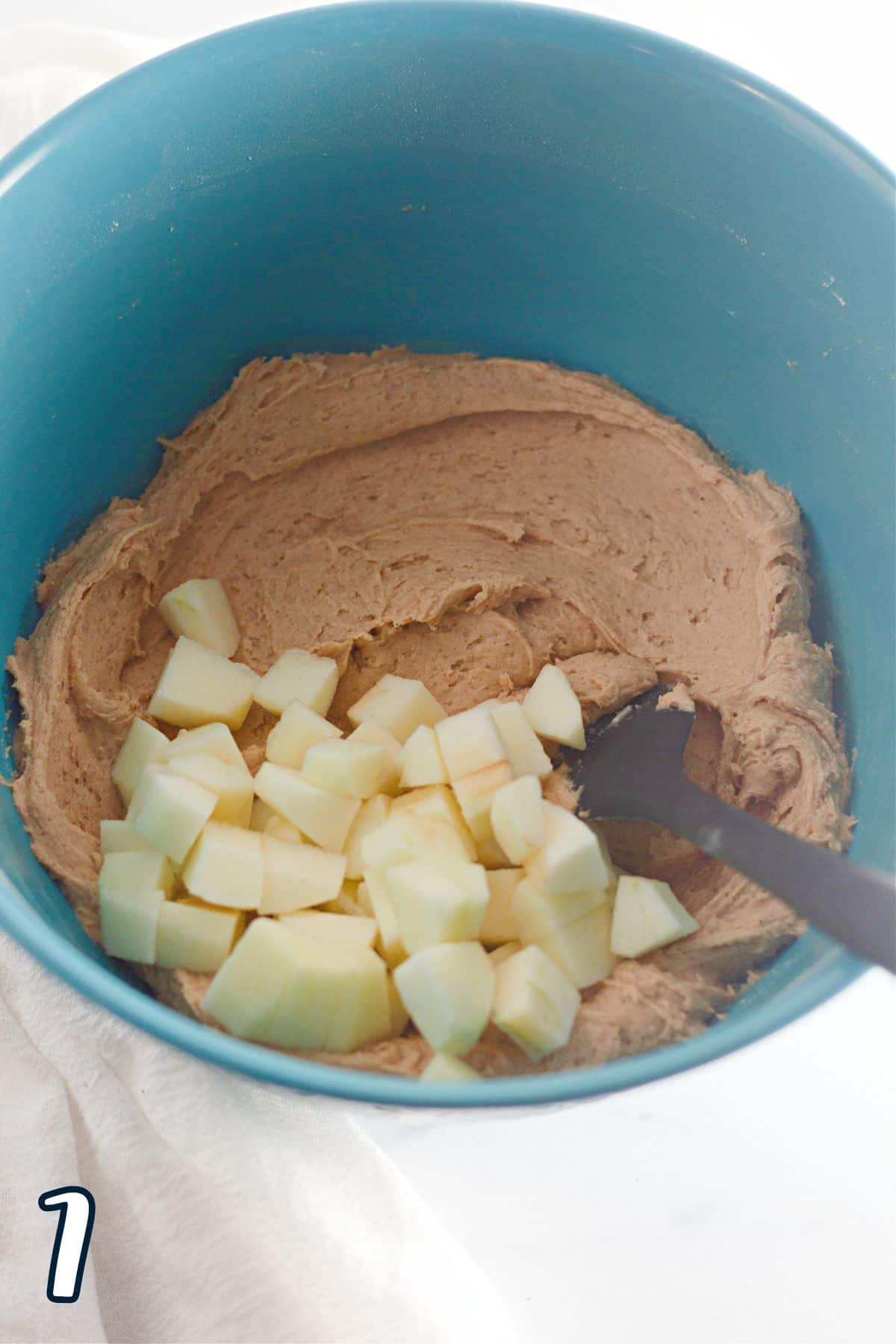 A blue bowl with apples on top of muffin batter. 