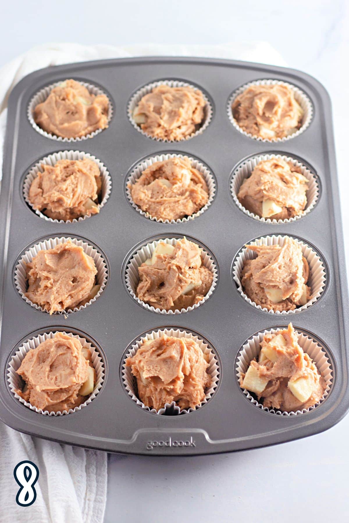 A muffin tin filled with apple muffin batter. 