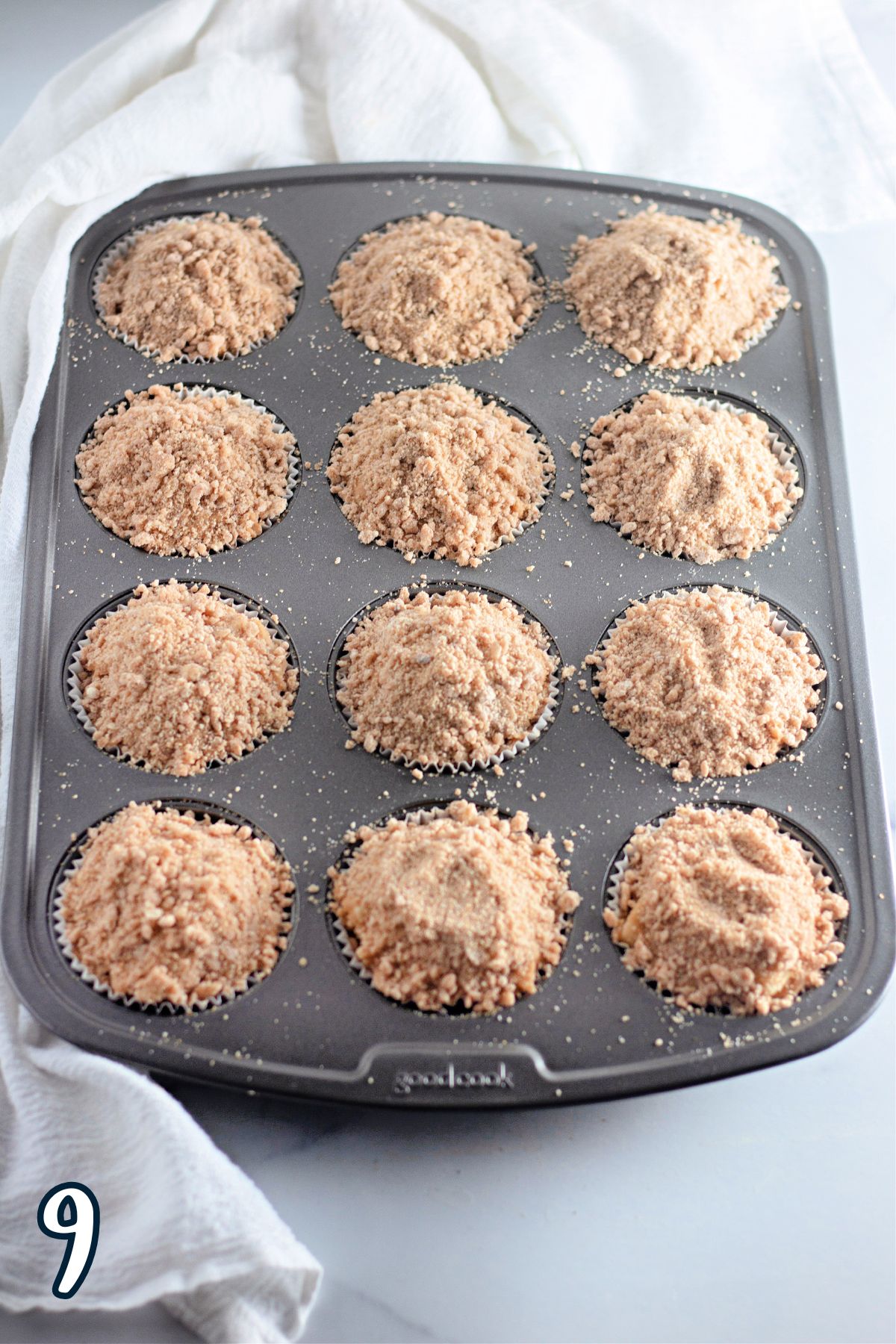 Crumb topping over apple muffin batter in a muffin tin. 