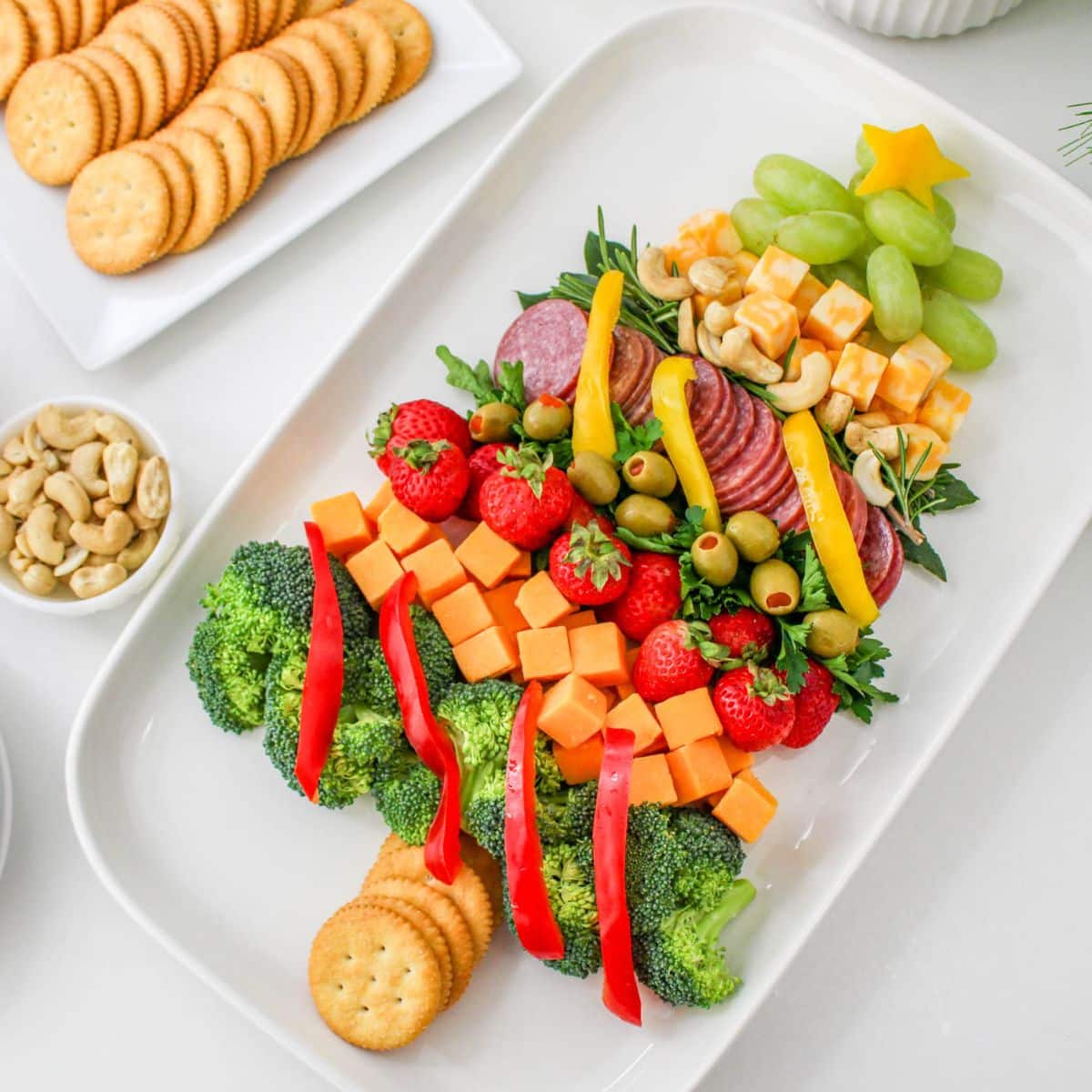 A christmas tree shaped platter of fruit and crackers.