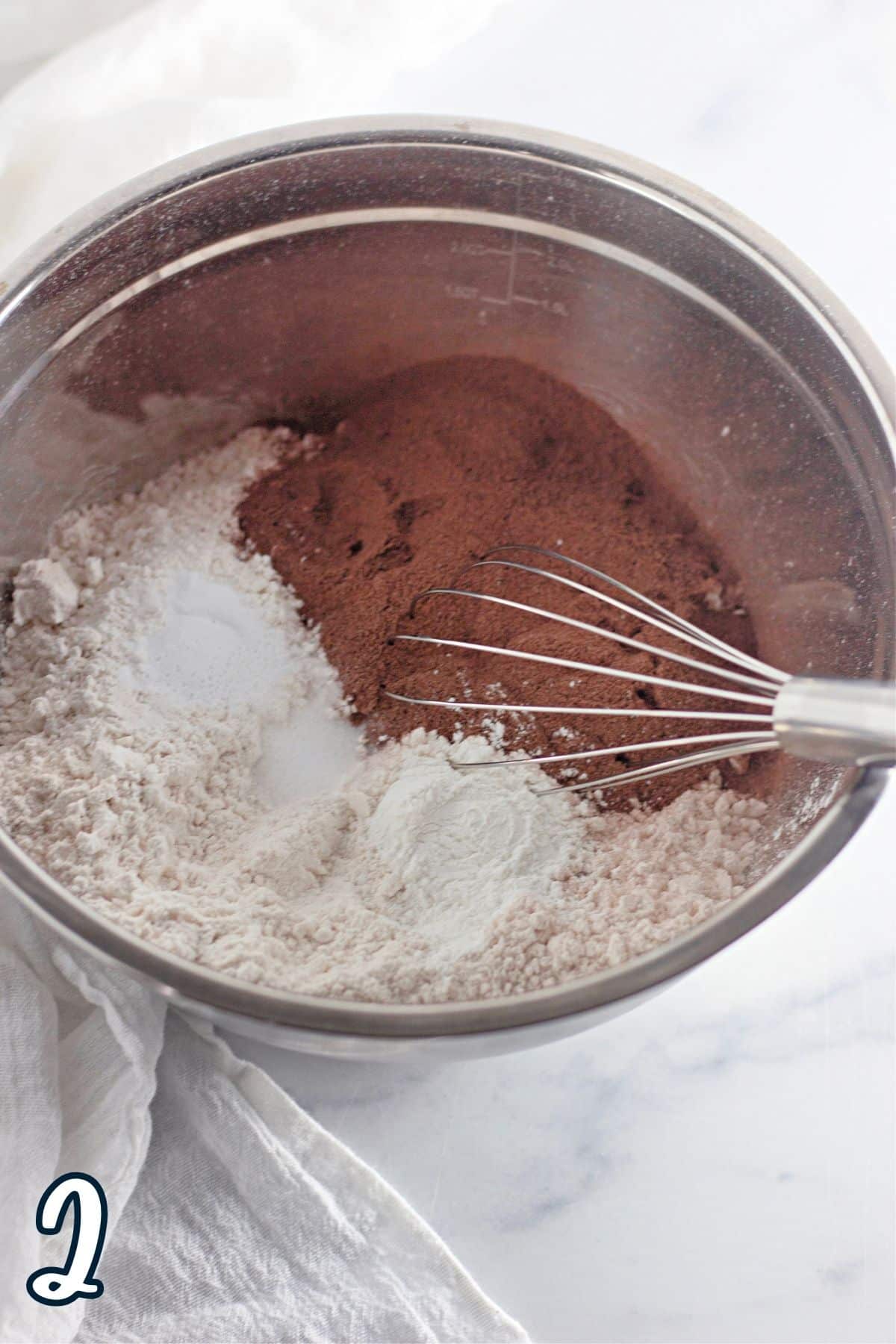 A metal bowl filled with flour, cocoa powder, other ingredients, and a whisk.