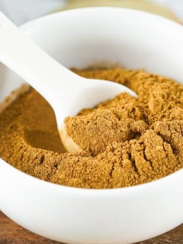 Pumpkin pie spice in a white bowl with a white spoon.
