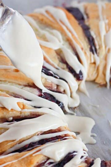 A spoon is drizzling icing on a pastry.