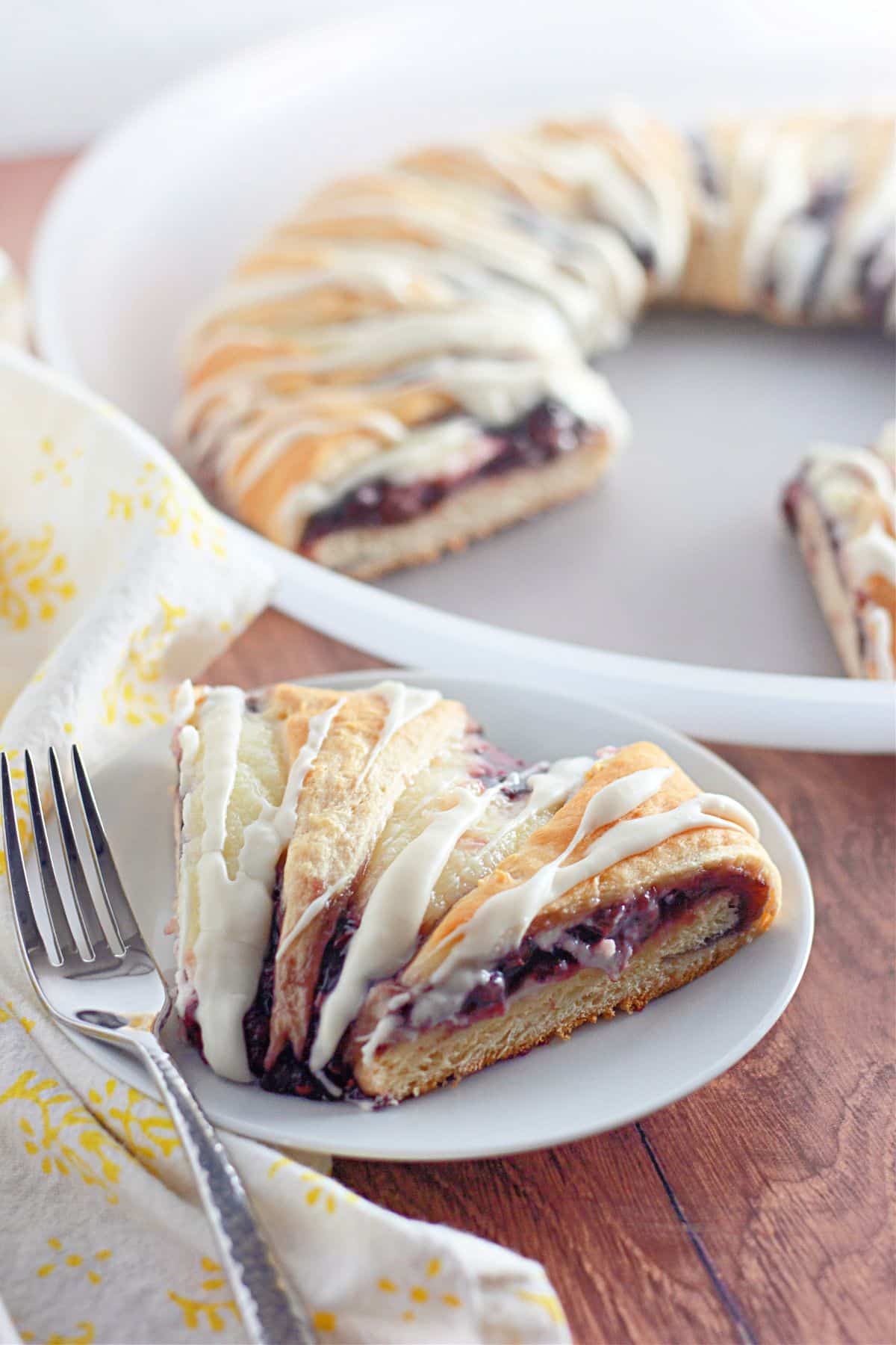 A slice of pastry filled with raspberry and cream cheese on a white plate next to a fork.