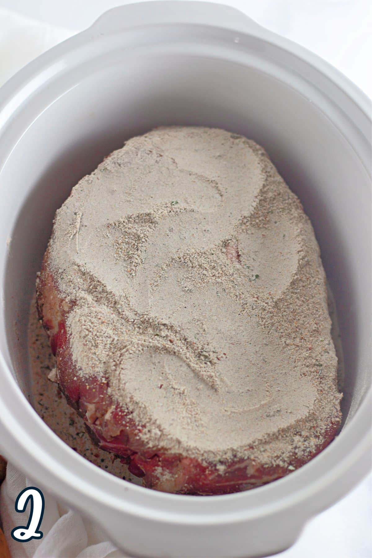 A crock pot with a seasoned piece of meat in it.