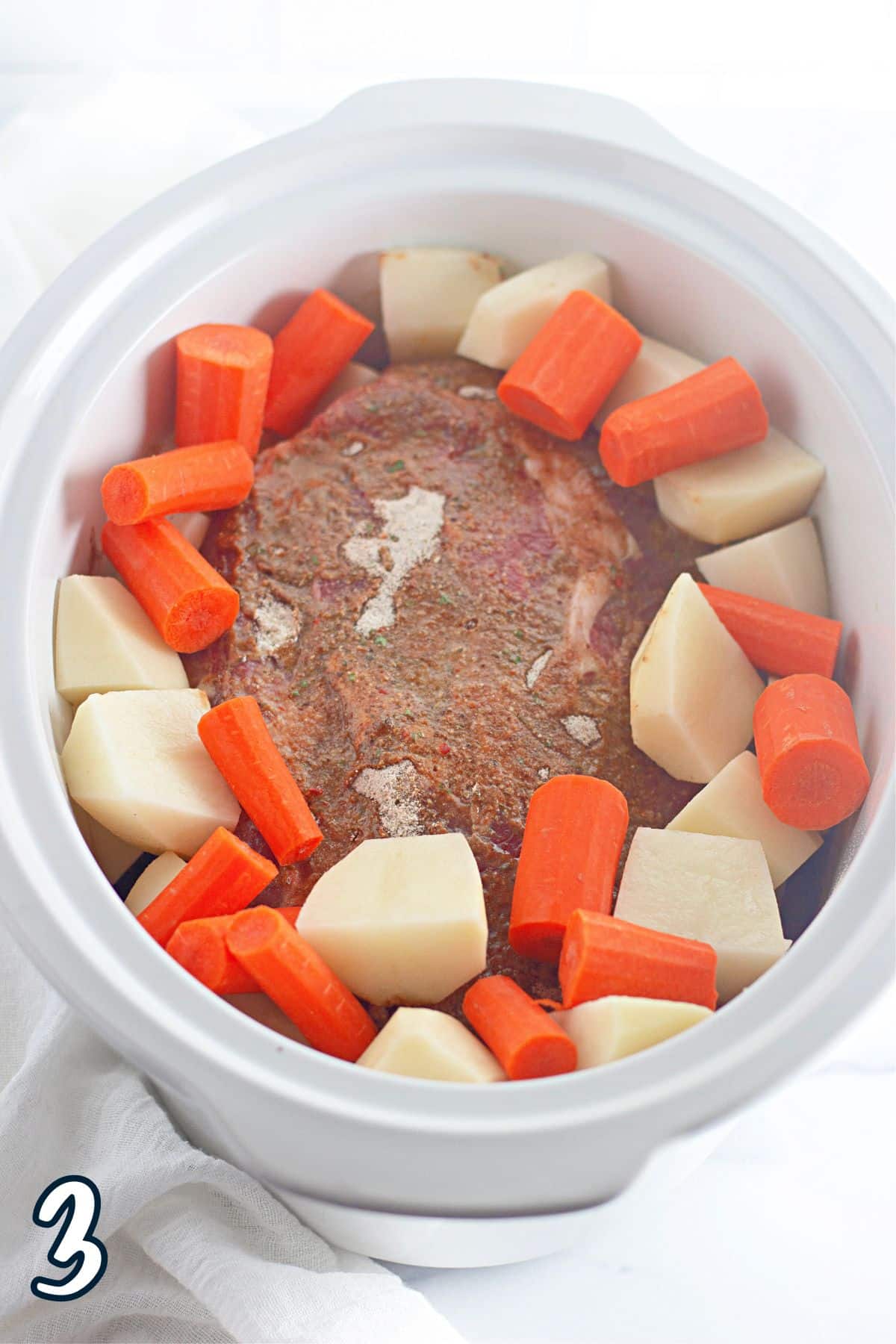 A white slow cooker bowl with carrots and meat in it.