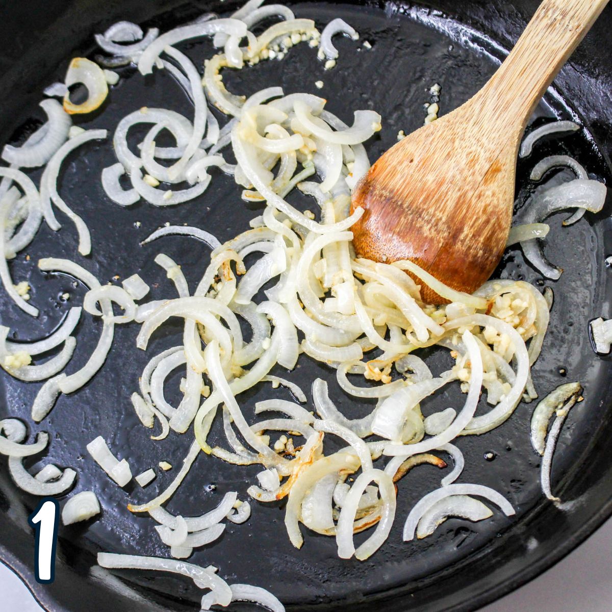 Onions in a pan with a wooden spoon.