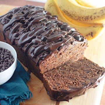 A slice of chocolate banana bread with glaze on a wood base.