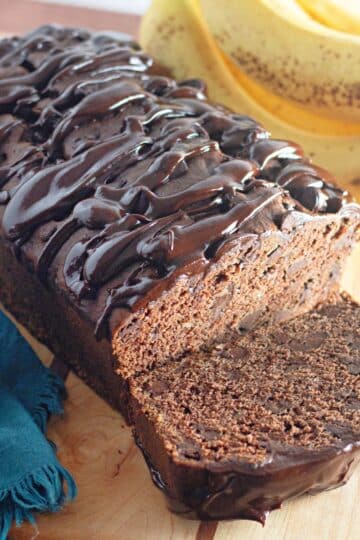 A slice of chocolate banana bread with glaze on a wood base.