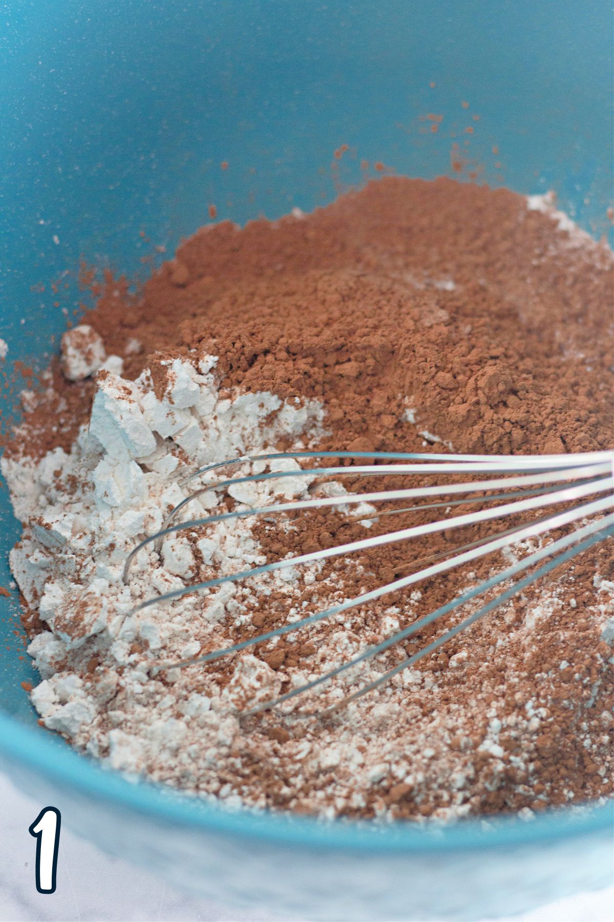 A blue bowl with flour, cocoa powder, and a whisk in it.