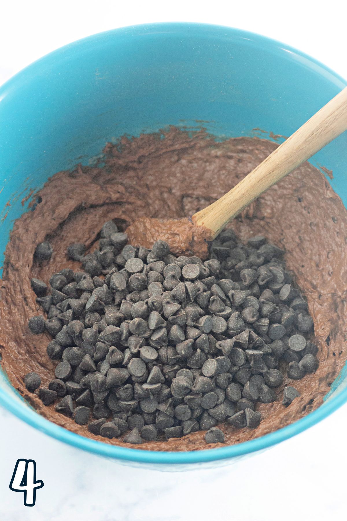 Chocolate banana bread batter and chocolate chips in a blue bowl with a wooden spoon.