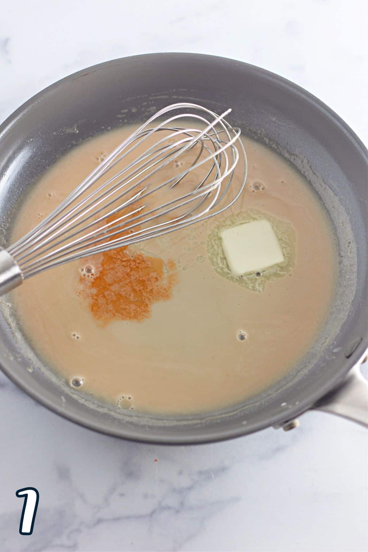 A frying pan with a whisk, heavy cream, brown sugar and butter in it.