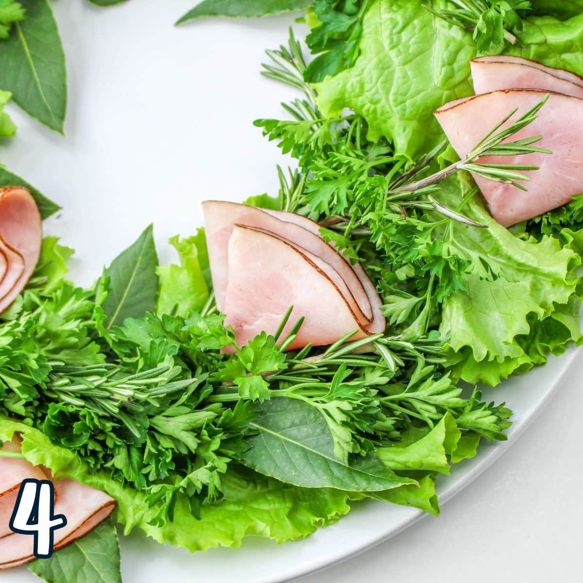A plate with ham, lettuce and herbs on it.
