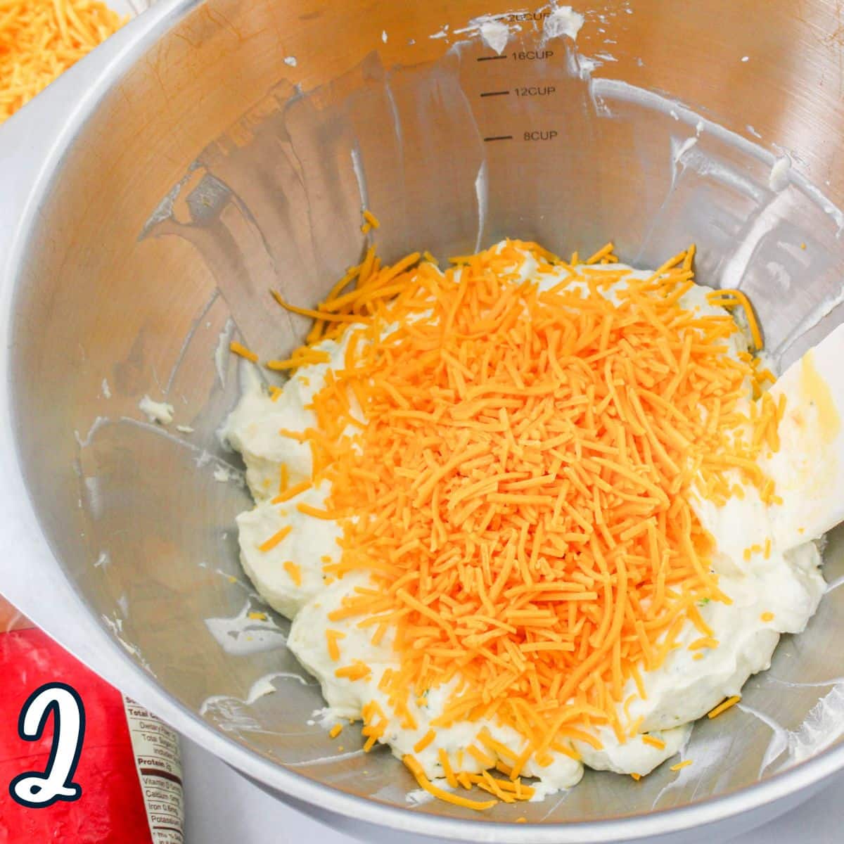 Shredded cheese added to a condensed soup and sour cream mixture in a mixing bowl. 