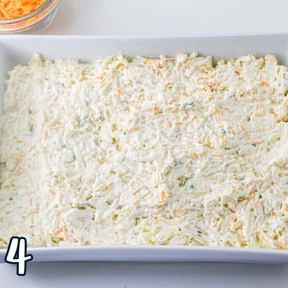 A white casserole dish filled with hashbrowns, cheeses, and a sour cream mixture. 