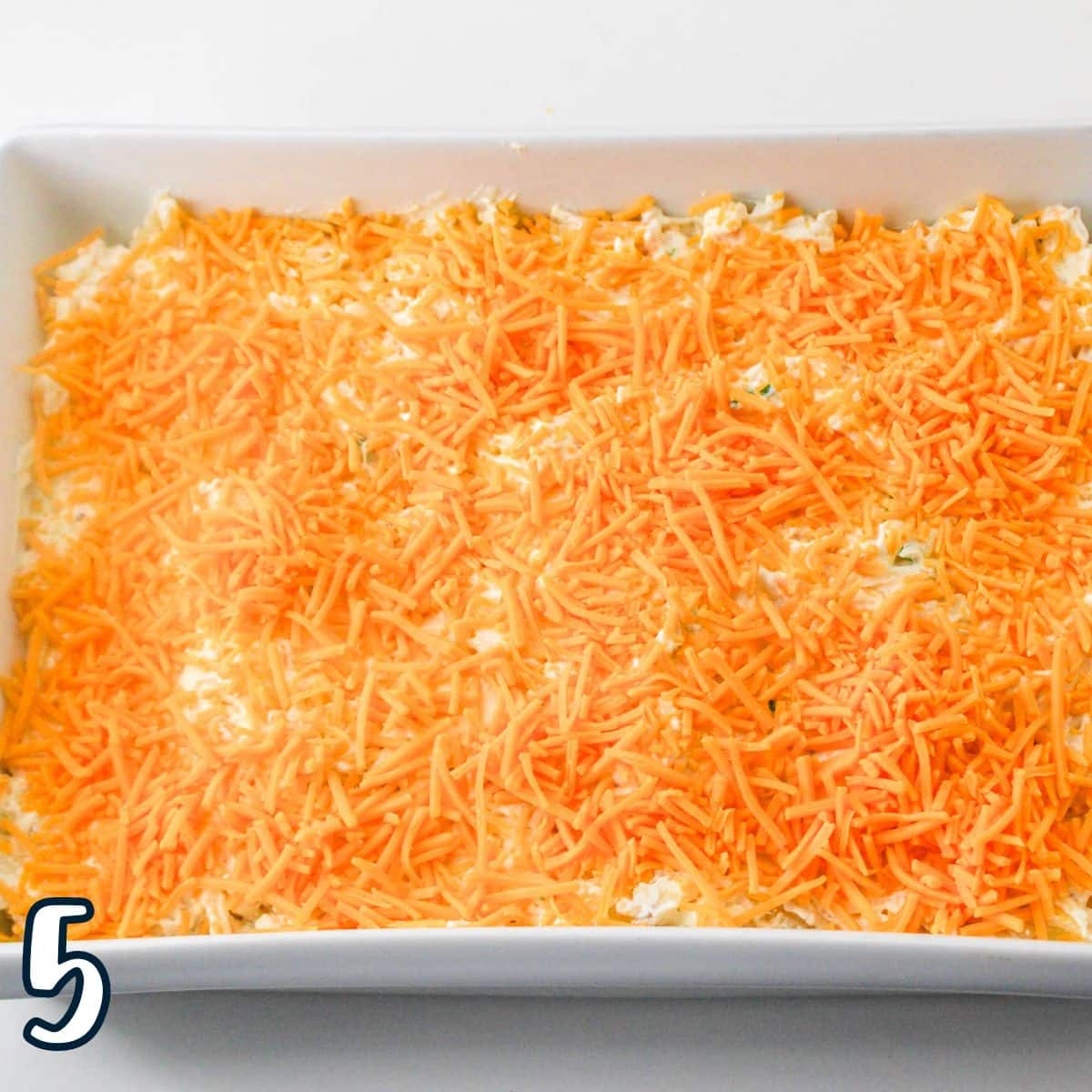 Shredded cheese sprinkled over cheesy hashbrowns in a white baking dish. 