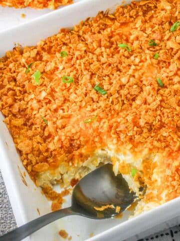 A white casserole dish full of hashbrown casserole with a serving spoon.