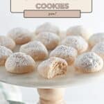 A cake stand displays cream cheese cookies dusted with powdered sugar; one cream cheese cookie has a bite taken out.