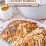 Sliced, seasoned Dutch Oven Turkey Breast is served on a white plate with rich gravy and fresh herbs beside a white Dutch oven.